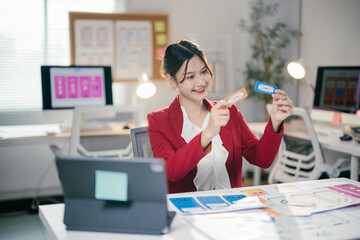 Smiling asian woman ux ui designer working on a new mobile application prototype, choosing between two options of design in her bright modern startup office