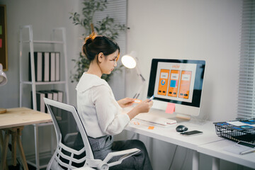 Young ui designer works on a mobile app in her home office, comparing colors with focus and surrounded by technology