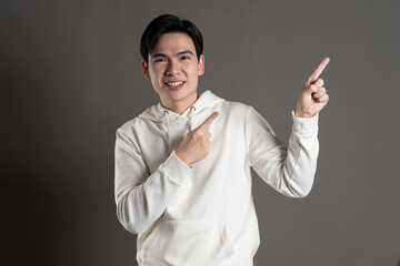 Portrait of Asian man wearing hoodie and posing on gray background.