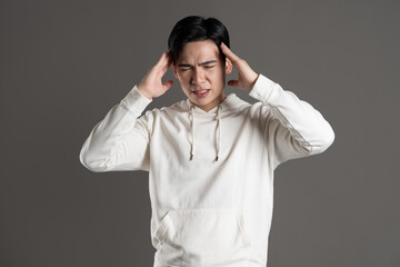 Portrait of Asian man wearing hoodie and posing on gray background.