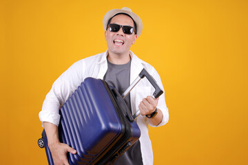 Excited Asian Traveler Man Wear Hat and Sunglasses Carrying Suitcase Isolated on Yellow Background