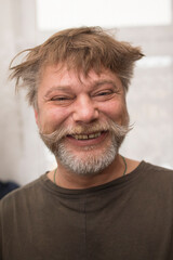 A man in a Tshirt with a beard and mustache is happily smiling for the camera, showing off his facial hair. His jawline and throat are visible, with a few wrinkles around his eyes