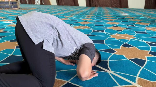 A Muslim man performing prayers in a mosque in a prostrate position.