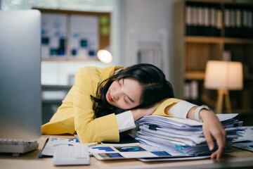 Young businesswoman wearing a yellow jacket is sleeping on a stack of paperwork at her desk after working late in the office