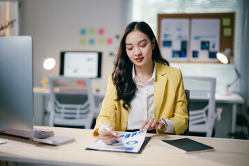 Young professional woman is reviewing financial data and using a pen while working on a report in her bright, modern office