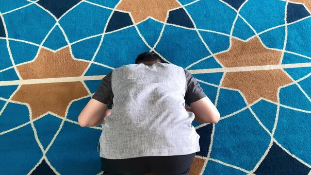 A Muslim man is performing prayers in a mosque in a prostrate position.