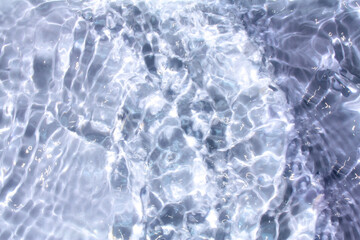 Fototapeta premium Bluewater waves on the surface ripples blurred. Defocus blurred transparent blue colored clear calm water surface texture with splash and bubbles. Water waves with shining pattern texture background. 
