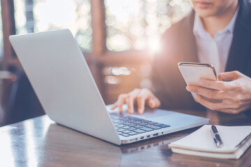 Businesswoman using mobile smart phone, working on laptop computer at office,woman using smartphone searching the information, surfing tne internet with laptop on office table.