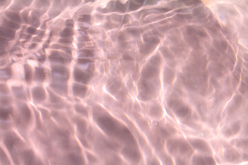 Pink water bubbles on the surface ripples. Defocus blurred transparent pink colored clear calm water surface texture with splash and bubbles. Water waves with shining pattern texture background