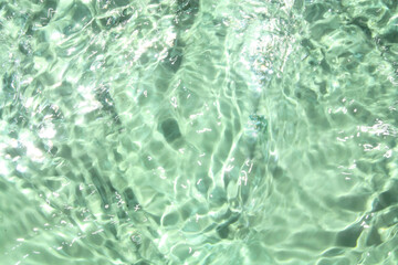 Fototapeta premium Defocus blurred transparent green colored clear calm water surface texture with splashes and bubbles. Trendy abstract nature background. Water waves in sunlight with copy space. Green water shine