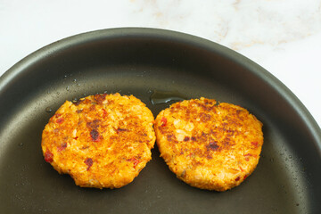 Two cooked salmon cakes in frying pan with olive oil