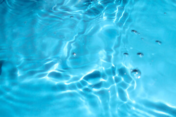Blue water with ripples on the surface. Defocus blurred transparent blue colored clear calm water surface texture with splashes and bubbles. Water waves with shining pattern texture background.