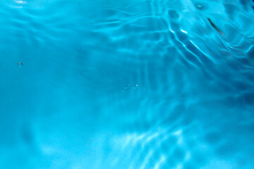 Blue water with ripples on the surface. Defocus blurred transparent blue colored clear calm water surface texture with splashes and bubbles. Water waves with shining pattern texture background.