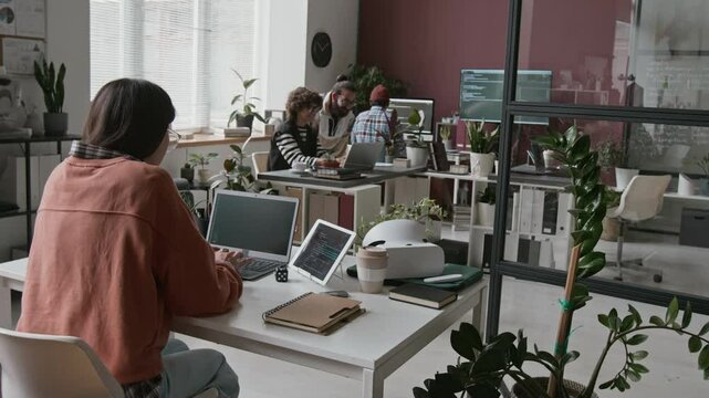 Timelapse footage of busy working day at IT company - female programmer sitting at desk, writing code on laptop, testing on tablet, making notes, diverse colleagues walking on errands around office