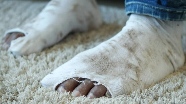 A detailed closeup of feet in worn and torn socks resting on a cozy carpet