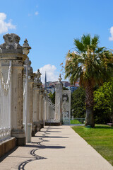 Fototapeta premium Elegant stone pillars and intricate iron gates in a sunny historical garden showcasing lush greenery and architectural beauty during the day