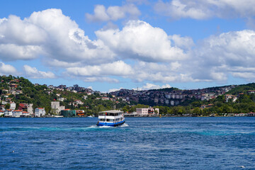Obraz premium Passenger ferry navigating the Bosphorus with scenic views of Istanbul\'s hills and coastline under a bright, partly cloudy sky