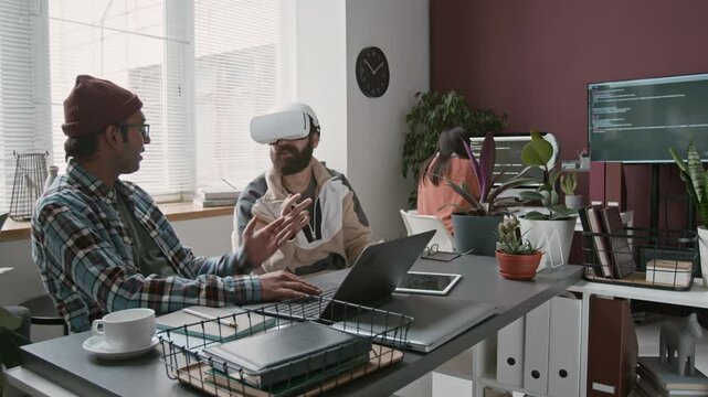 Medium timelapse looped footage of two multiethnic male software developers and collaborating on virtual reality project, Indian programmer typing code on laptop, Arab colleague testing in AR headset