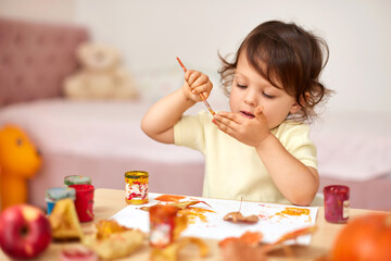 smiling little child girl painting her hands and autumn leaves. baby girl drawing hands in yellow paint