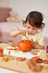 happy little child girl painting Halloween pumpkin. smiling baby girl drawing autumn pumpkin in yellow paint