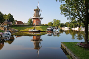 Reflections of a windmill and boats on canals (Driepypstergracht) in Dokkum, Friesland, Netherlands