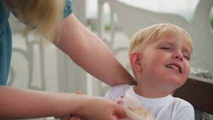 A young boy struggles as his mother gently wipes his mouth clean with a tissue