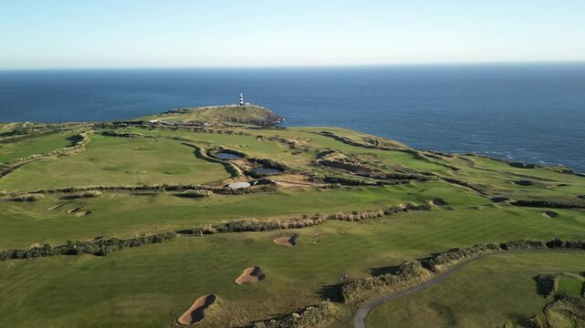 Green headland pointed to calm blue Atlantic Ocean, with protruding lighthouse. Old Head of Kinsale golf course, county Cork, Ireland aerial.
