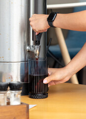 A person is pouring a drink into a glass from a dispenser