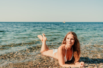 A woman is laying on the beach in a bikini, looking at the water