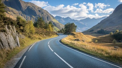 Fototapeta premium Scenic winding road through mountains in beautiful landscape under a blue sky with fluffy clouds.