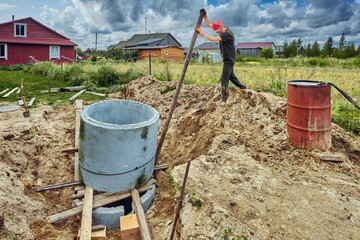 Builder places one concrete ring on top of another and levels it with lever using steel pipe when building septic tank.