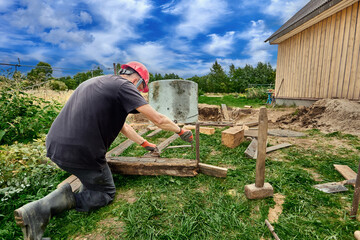 Worker lowers concrete ring into pit using hand winch during construction of septic tank.