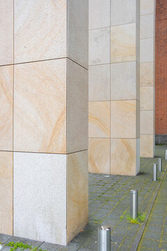 Close-up shot of large stone pillars supporting a modern building, showcasing the detailed texture and geometric pattern of the materials used in the architecture.
