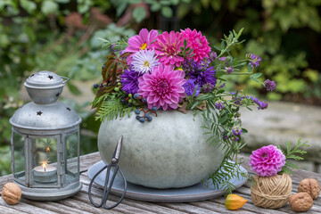 Herbst-Arrangement mit einem grauen Kürbis dekoriert mit Blumenkranz 