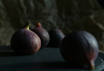Purple figs on a black stone plate. Photo, background with fresh, juicy, ripe tropical fruits. Suitable for depicting vegetarian and raw, healthy food, harvest. Symbol of abundance and enlightenment.