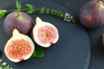 Purple figs on a black stone plate. Photo, background with fresh, juicy, ripe tropical fruits. Suitable for depicting vegetarian and raw, healthy food, harvest. Symbol of abundance and enlightenment.