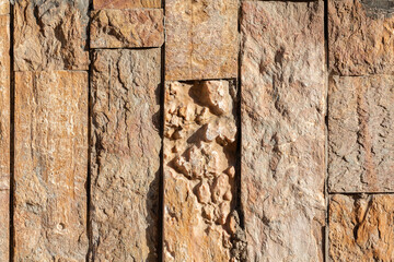 Close-up of a rugged stone wall with various textures and shades of beige and brown, showcasing natural formations and rough surfaces