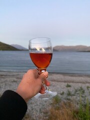 Hand holding a glass of wine with lake views at the background 