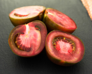 Black halves of tomatoes on black stone board