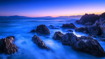 Obraz premium A serene coastal landscape at dusk, featuring rocky formations and gentle waves under a twilight sky.