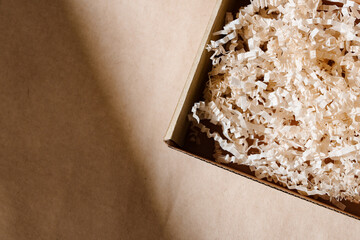 Open cardboard box with shredded paper packaging resting on a light brown surface illuminated by soft natural light