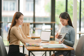 Two women work with tablets,  work and chatting about paperwork and graphs.