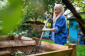 Senior woman shoveling compost with a pitchfork in the garden
