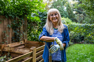 Senior woman standing with a pitchfork in front of the compost heap in the garden