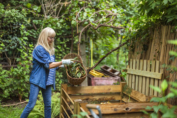 Senior woman throwing vegetable scraps into a compost heap in the backyard