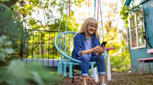 Mature woman using mobile phone while sitting on a swing in the garden
