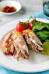 Red prawns or tiger prawns on a white plate with greens and tomatoes. Tiger shrimps