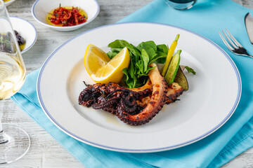 Grilled octopus with arugula and mini vegetables on a white porcelain plate