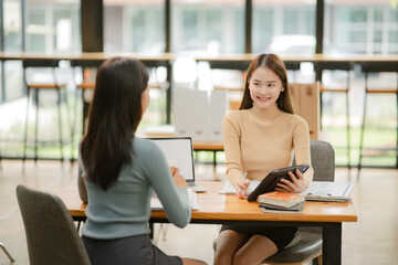 Two women work with tablets,  work and chatting about paperwork and graphs.