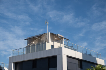 side view of a modern architecture individual house with an installation of photovoltaic solar panels with a light glass railing. The day is sunny. Concept of sustainable, clean, and renewable energy